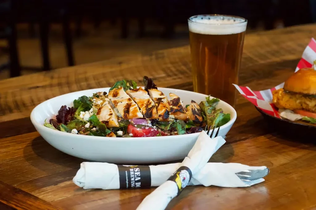 Grilled chicken salad, beer, and cutlery with Sea Dog Brewing logo.