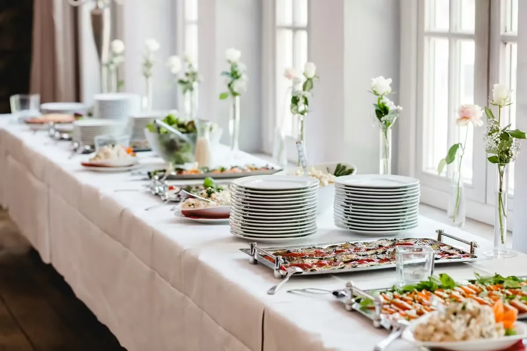 Well-lit buffet table featuring diverse food, clean plates, and flower decor.
