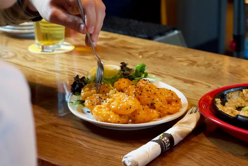 Hand forks crispy shrimp with orange sauce on a wooden table.