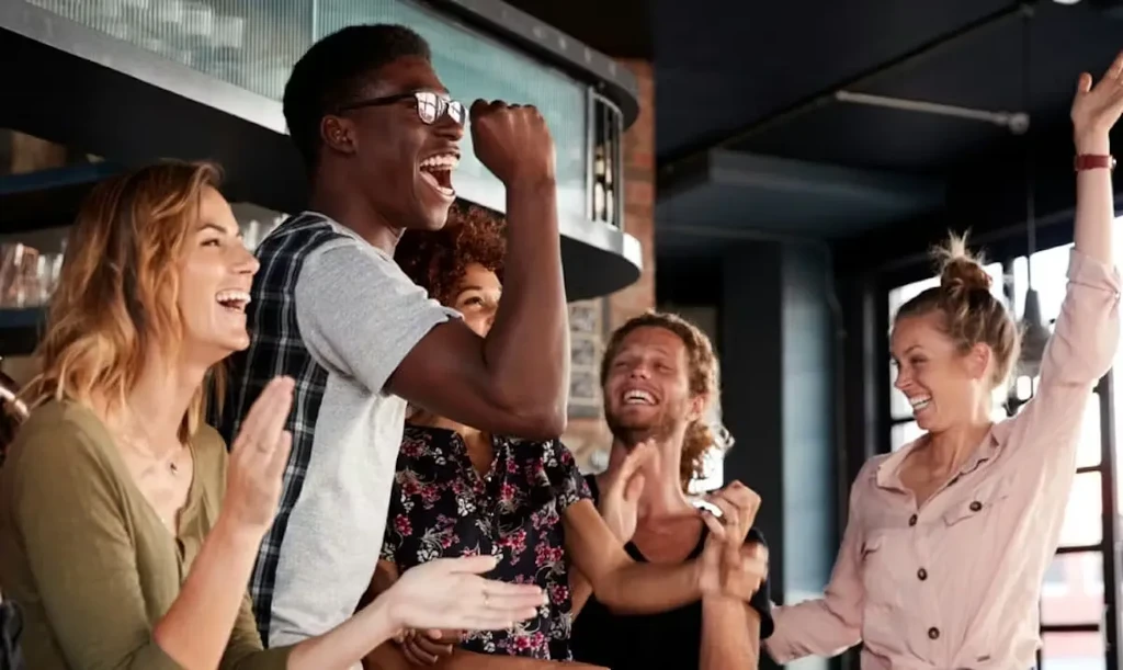 Five diverse people celebrating joyfully with laughter and raised arms.