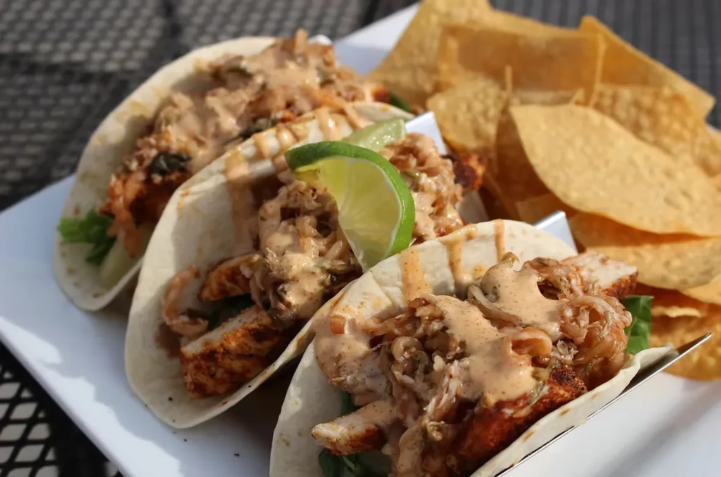 Three soft-shell chicken tacos with lettuce, sauce, lime, and chips.