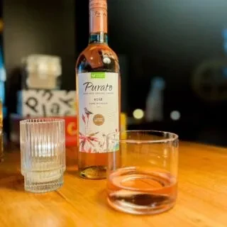 Purato rosé wine bottle, two tumblers, on a wooden bar top.