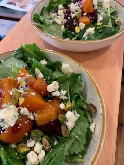 Two bowls of colorful salads with greens, roasted vegetables, cheese, nuts.