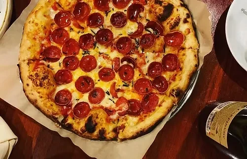 Wood-fired pepperoni pizza, generously topped with cheese and green herbs.