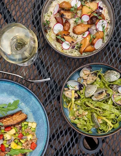 Three vibrant gourmet dishes and white wine on a dark table.