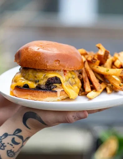 Burger and fries on a plate, held by a tattooed hand.