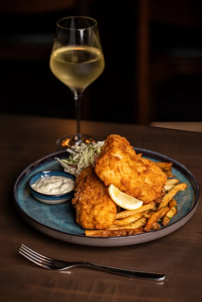 Plate of golden fish and chips with lemon, coleslaw, and tartar sauce.