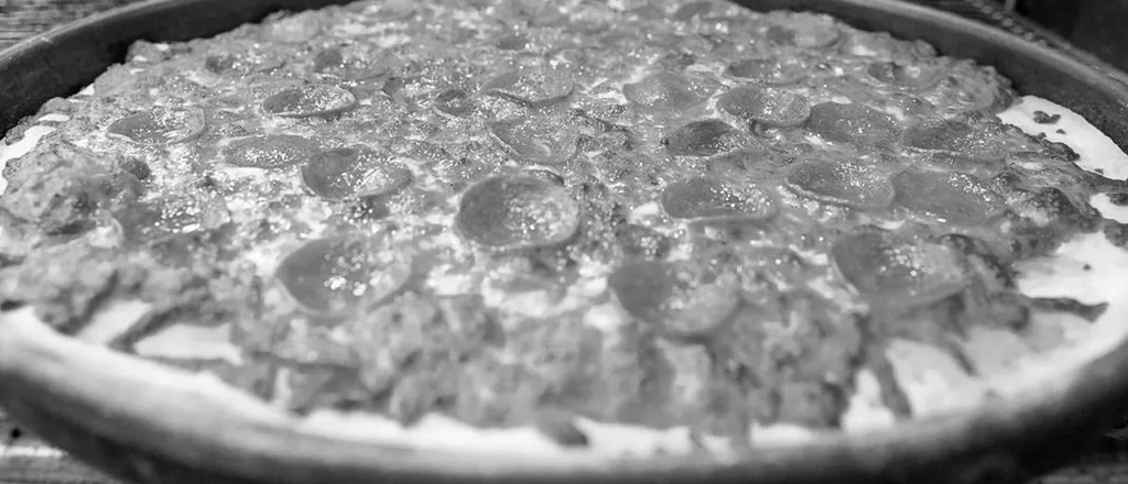 Black and white close-up of deep-dish pepperoni and cheese pizza.