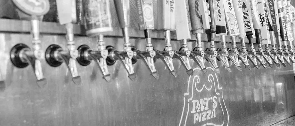 Numerous black and white beer taps on Pat's Pizza bar wall.