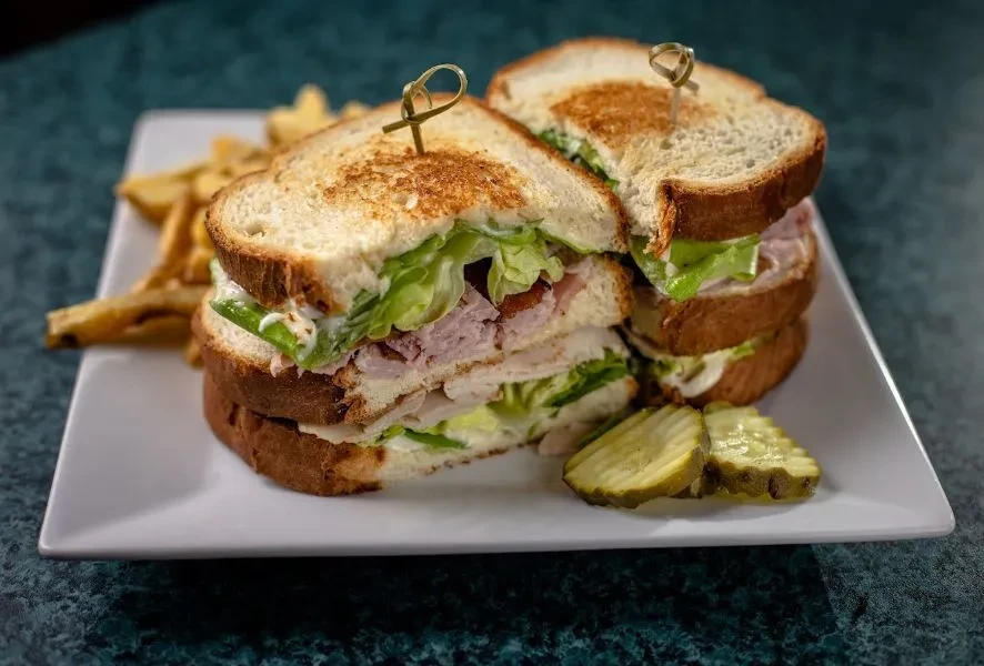 Double-decker club sandwich, fries, and pickle slices on a plate.