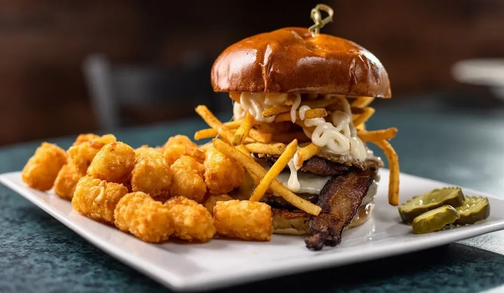 Large gourmet burger with bacon, egg, fries, tater tots, and pickles.