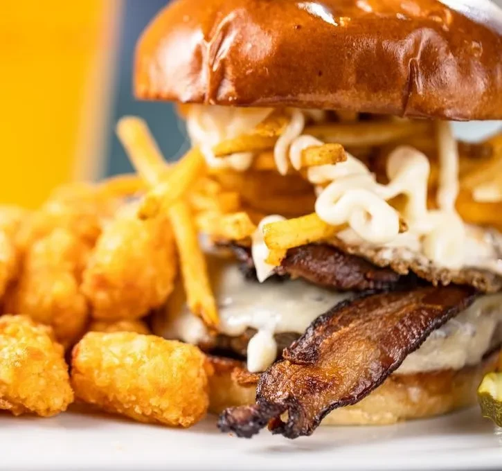 A gourmet burger topped with bacon, egg, cheese, fries, and tots.