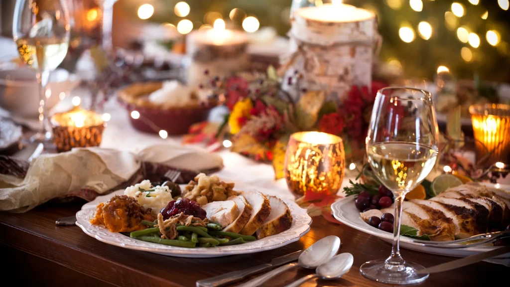 Two plates of holiday turkey dinner, wine, lit candles, and autumn decor.