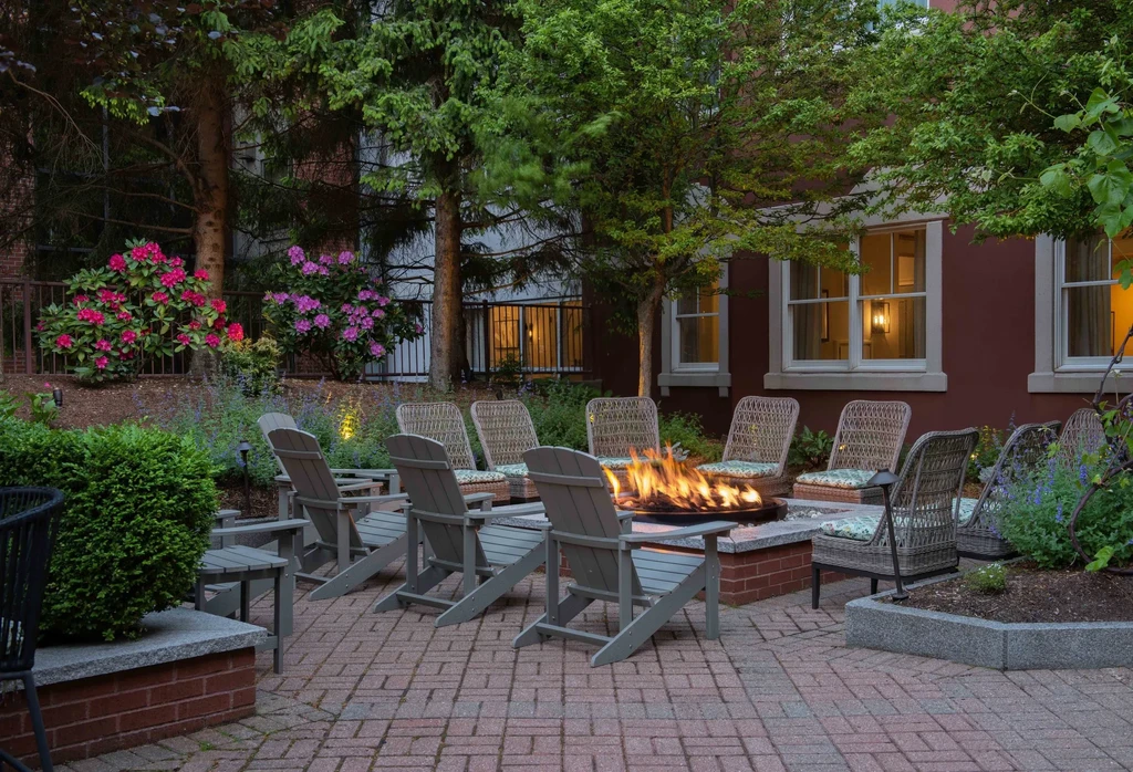 Dusk patio with fire pit, Adirondack chairs, and lush flowering shrubs.