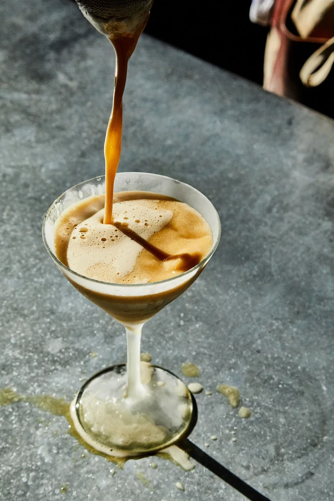 Golden-brown liquid streams into a martini glass, creating a swirl.