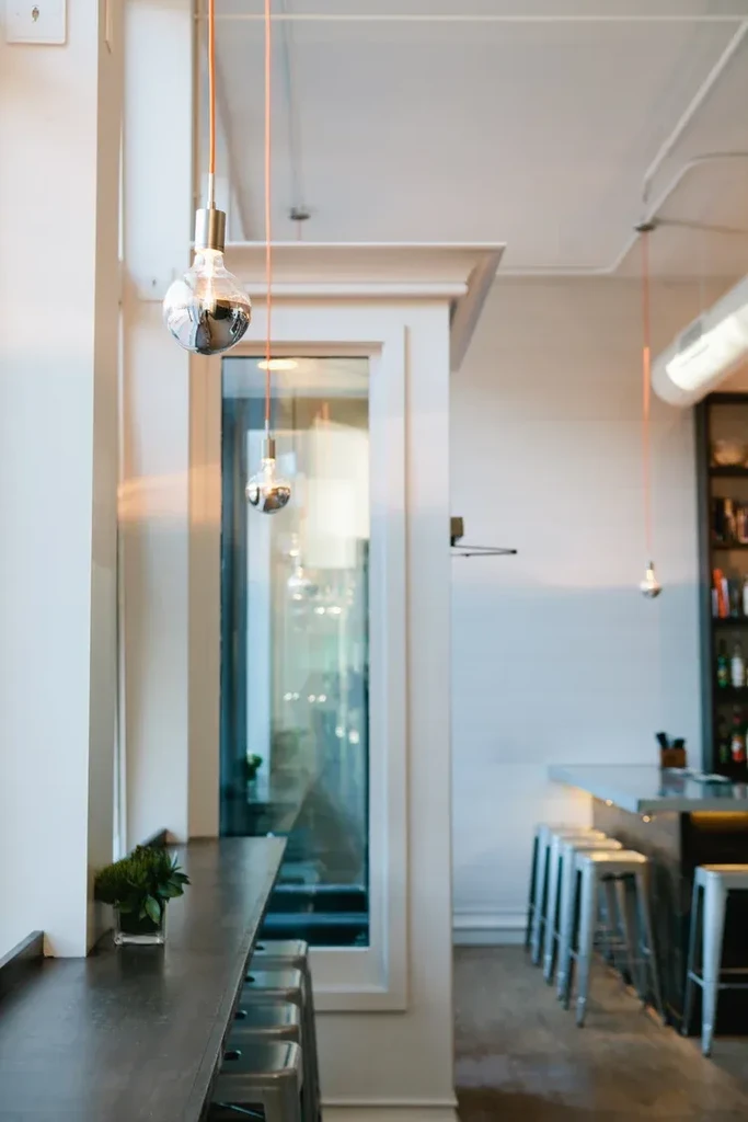 Modern bar interior with dark wooden counter, metal stools, and pendant lights.