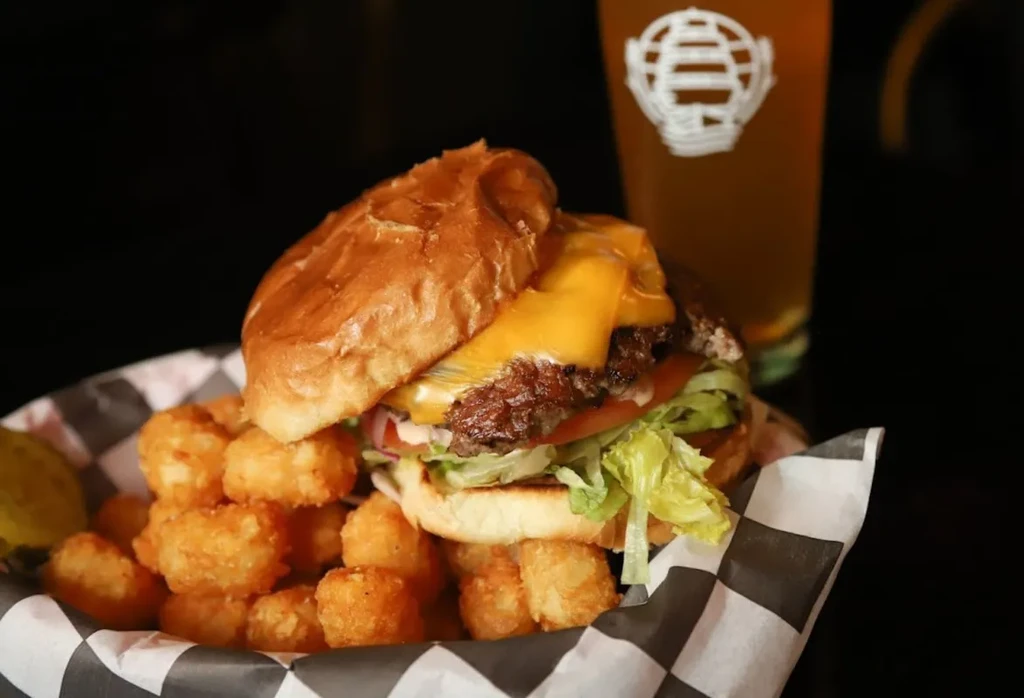 Cheeseburger, golden tater tots, and a pickle spear in a basket.