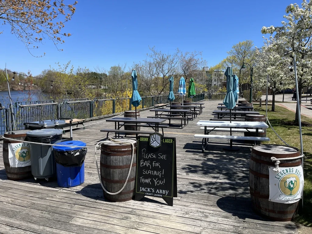 Empty sunny taproom patio with picnic tables and a river view.