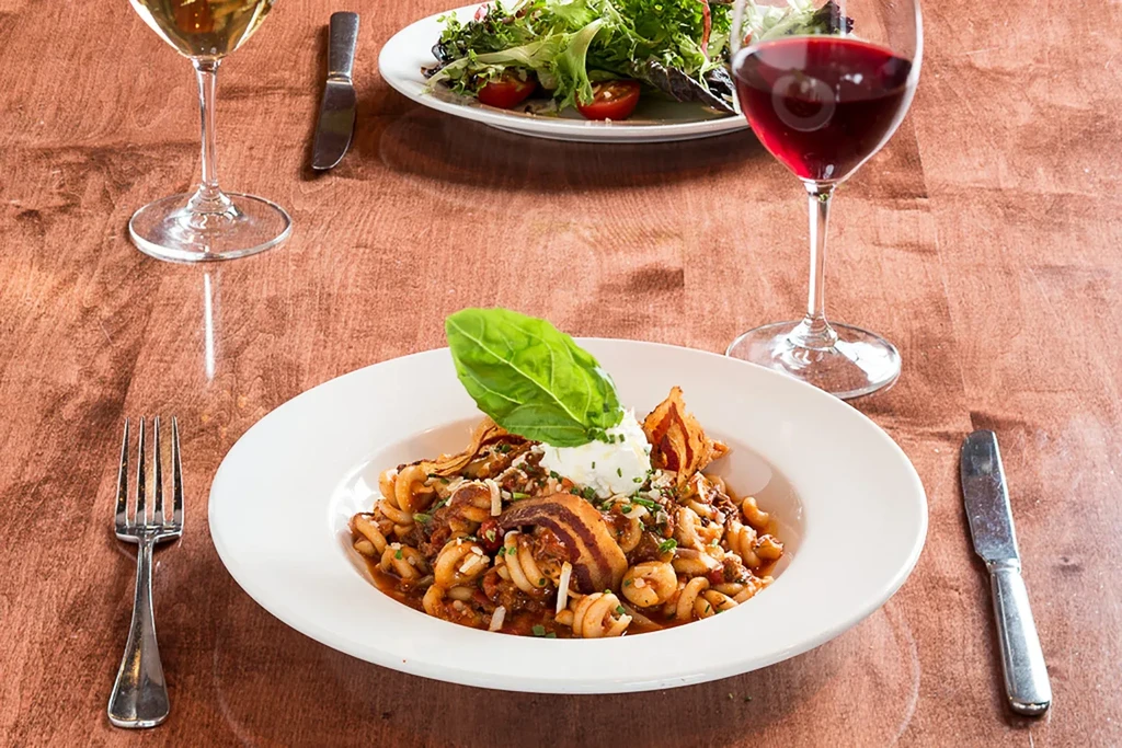 Top-down view of pasta, salad, and wine on a restaurant table.