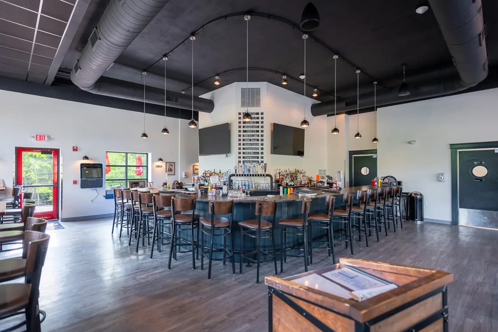 Empty, modern bar interior with large central bar, liquor display, and TVs.