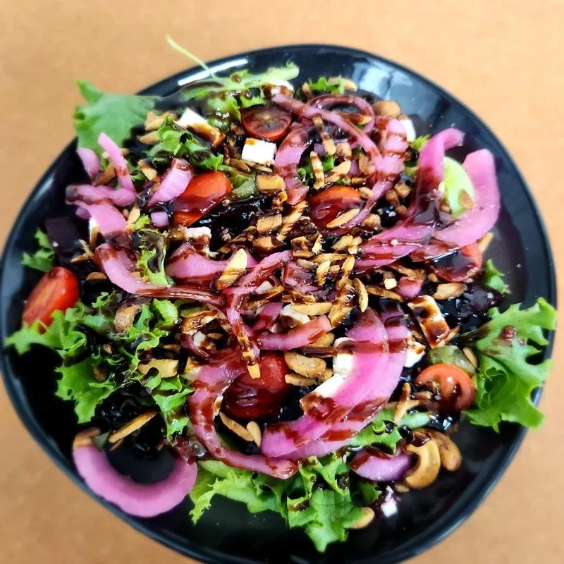 Colorful salad with lettuce, tomatoes, onions, cheese, nuts, balsamic glaze.