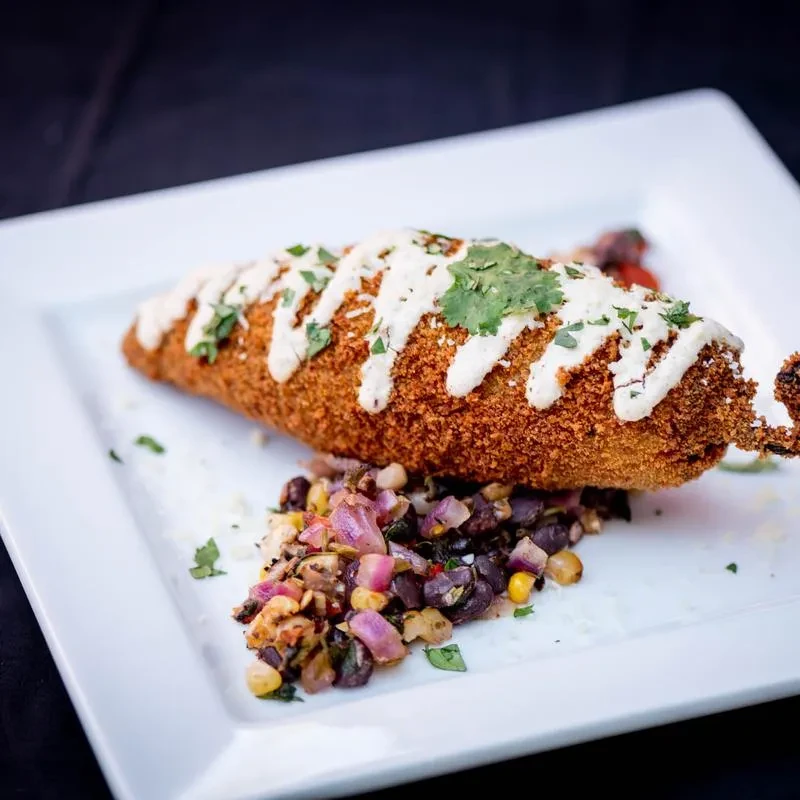 Crispy fried dish drizzled with crema, garnished with herbs, cheese, and salsa.