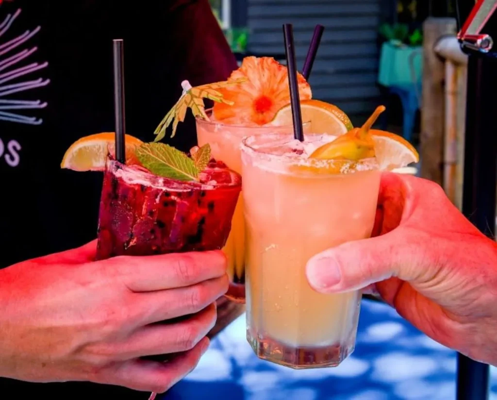 Three vibrant, garnished cocktails held in a group toast.
