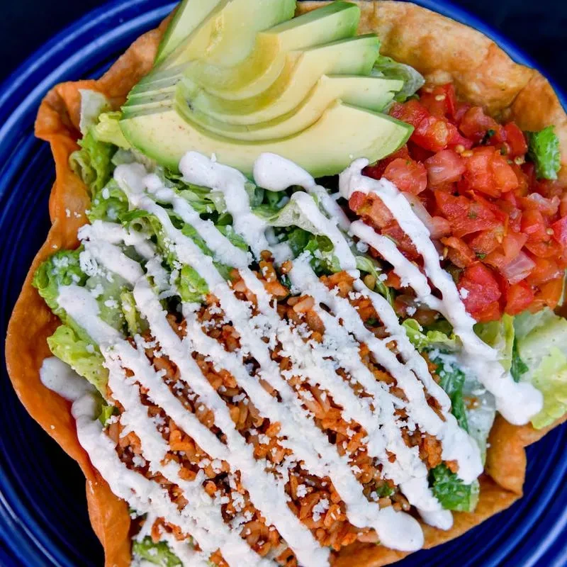 Taco salad in crispy tortilla bowl with avocado, pico, and cheese.