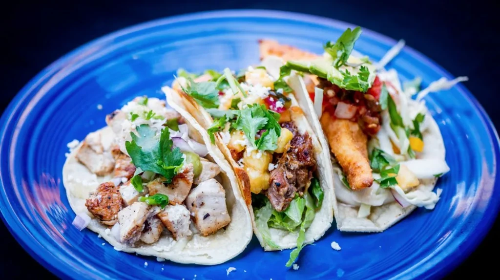Three distinct tacos with chicken, pork, and fish fillings.