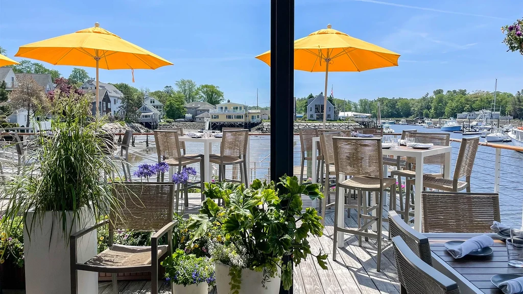 Vibrant waterfront dining patio with yellow umbrellas and potted plants.