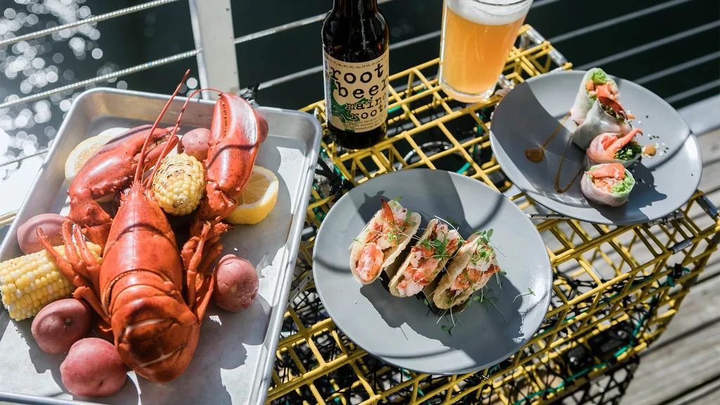 Cooked lobster, seafood tacos, drinks on yellow traps by water.