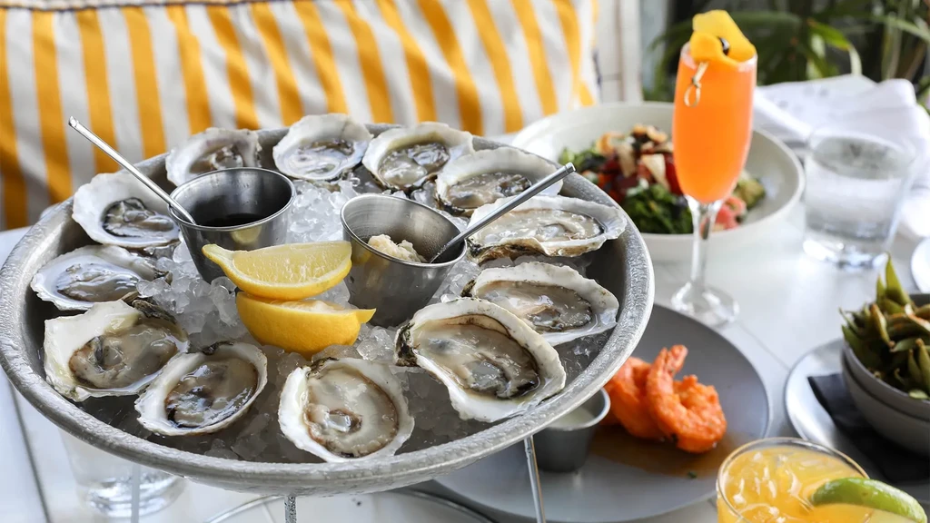Silver platter of fresh oysters on ice, with lemons and sauces.