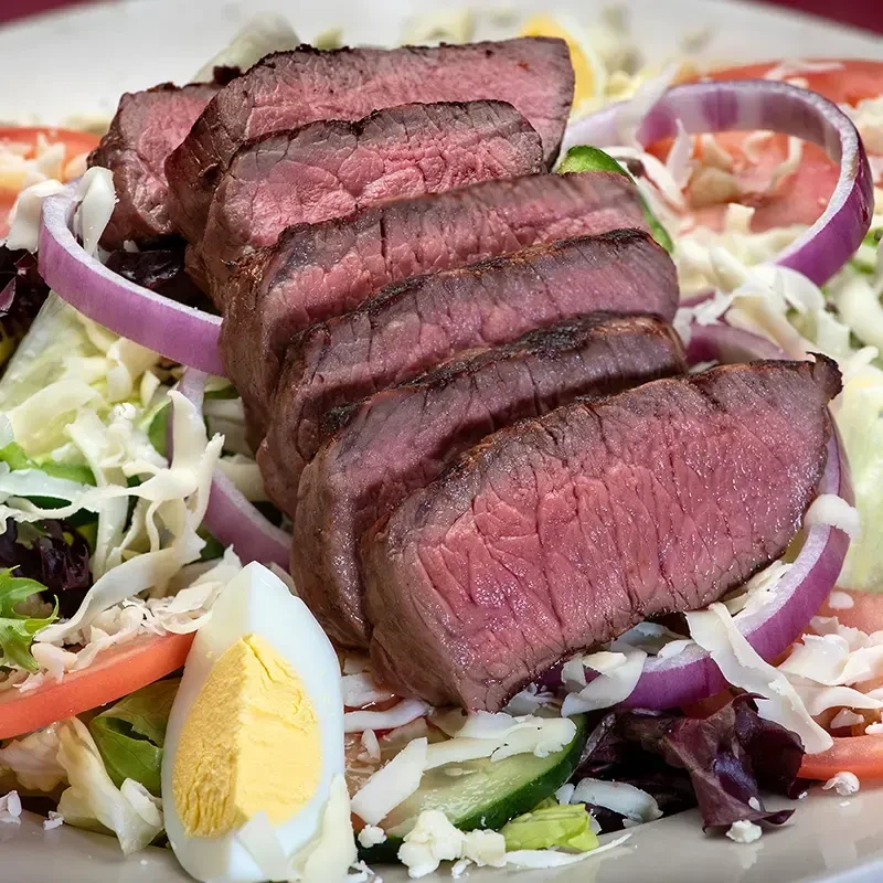 Medium-rare steak salad with mixed greens, vegetables, and a hard-boiled egg.