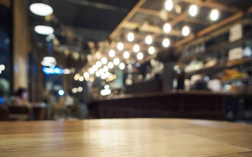 Sharp wooden table foreground, blurred restaurant background with warm bokeh lights.