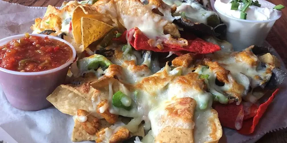 Close-up nachos with melted cheese, chicken, jalapeños, salsa, and sour cream.