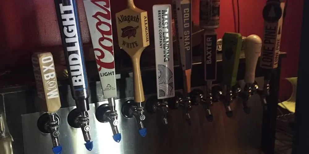 Nine distinct beer tap handles on a bar's metallic tap system.
