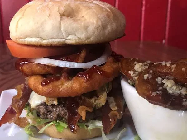 Gourmet hamburger with bacon, onion rings, sauce, and potato wedges.