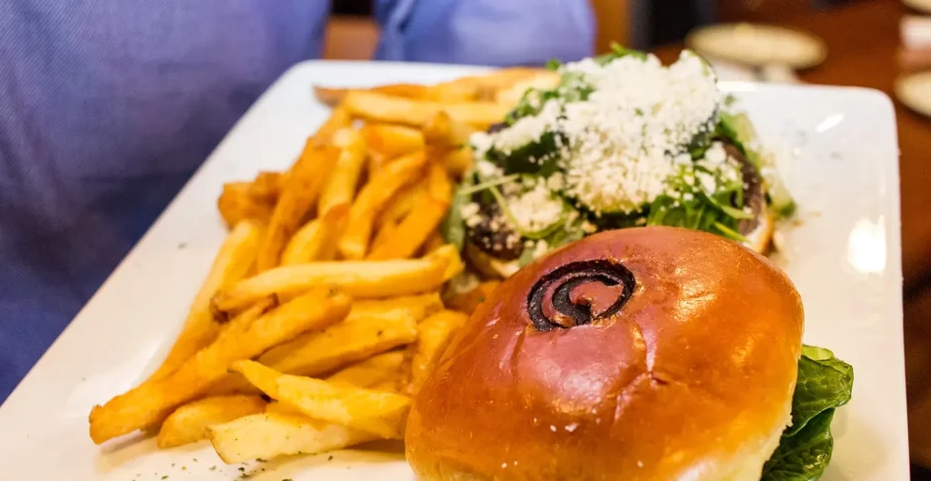 Burger with swirled bun, fries, and cheese-topped side salad on a white plate.
