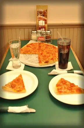 A dining table with a half-eaten pepperoni pizza, drinks, and condiments.