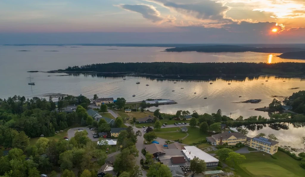 Aerial photo of coastal settlement, green forests, boats, and sunrise/sunset.