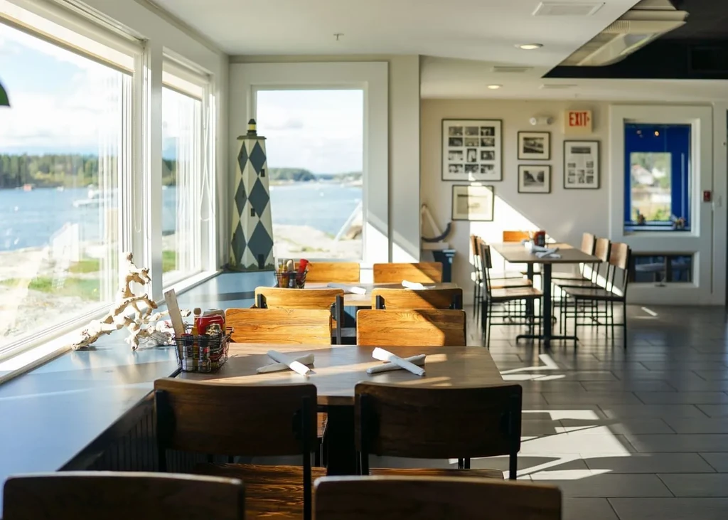Coastal restaurant interior with tables overlooking water and forest.