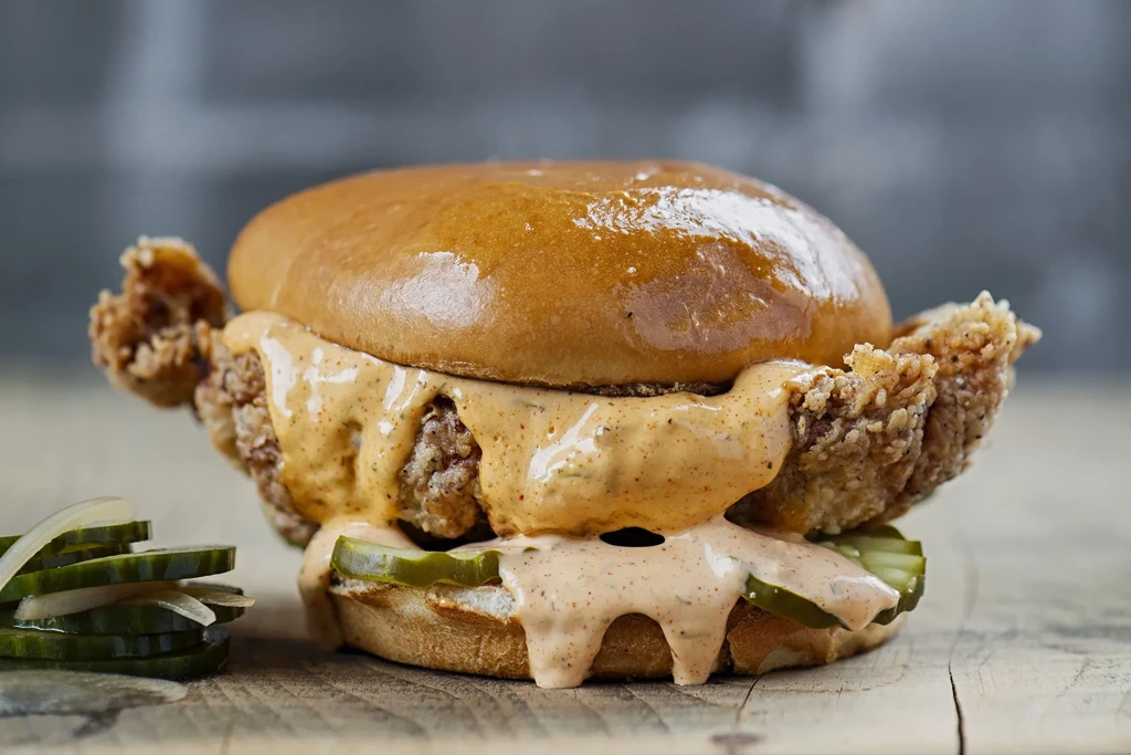 Crispy fried chicken sandwich, brioche bun, sauce, pickles on rustic wood.