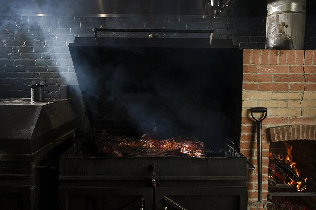 Large meat smoking in an industrial smoker near an active fireplace.