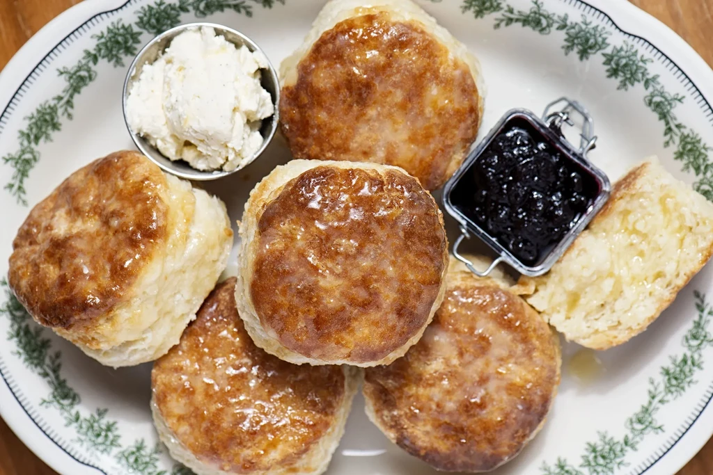 Platter of six golden biscuits, clotted cream, and berry jam.