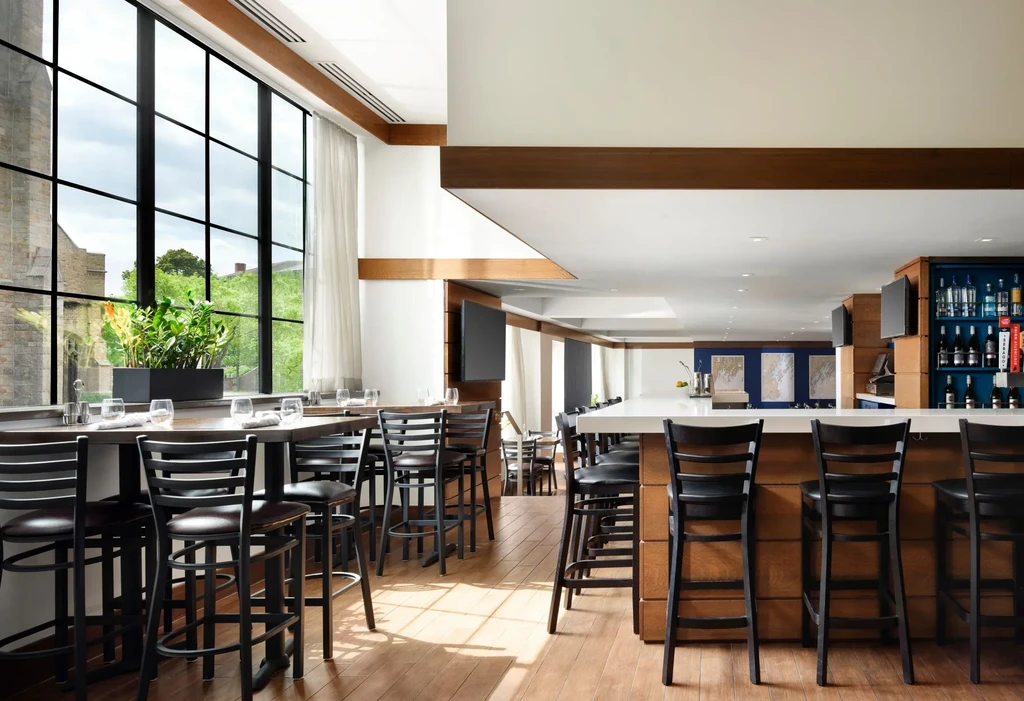 Modern bar interior with wooden counters, black stools, and large windows.
