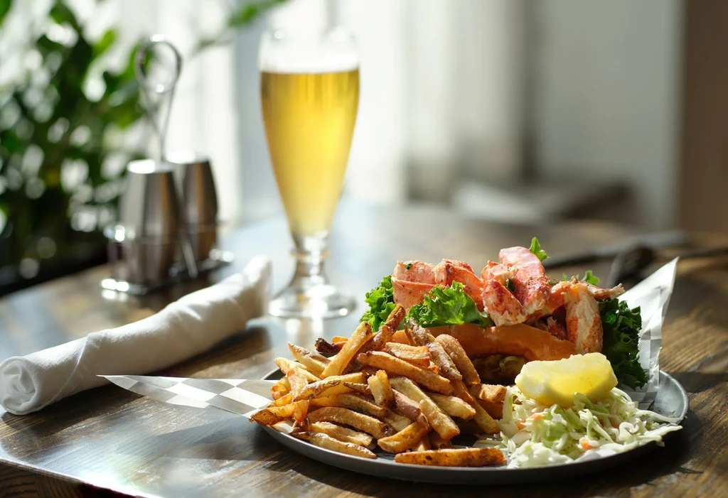 Lobster roll, french fries, coleslaw, and beer on a table.