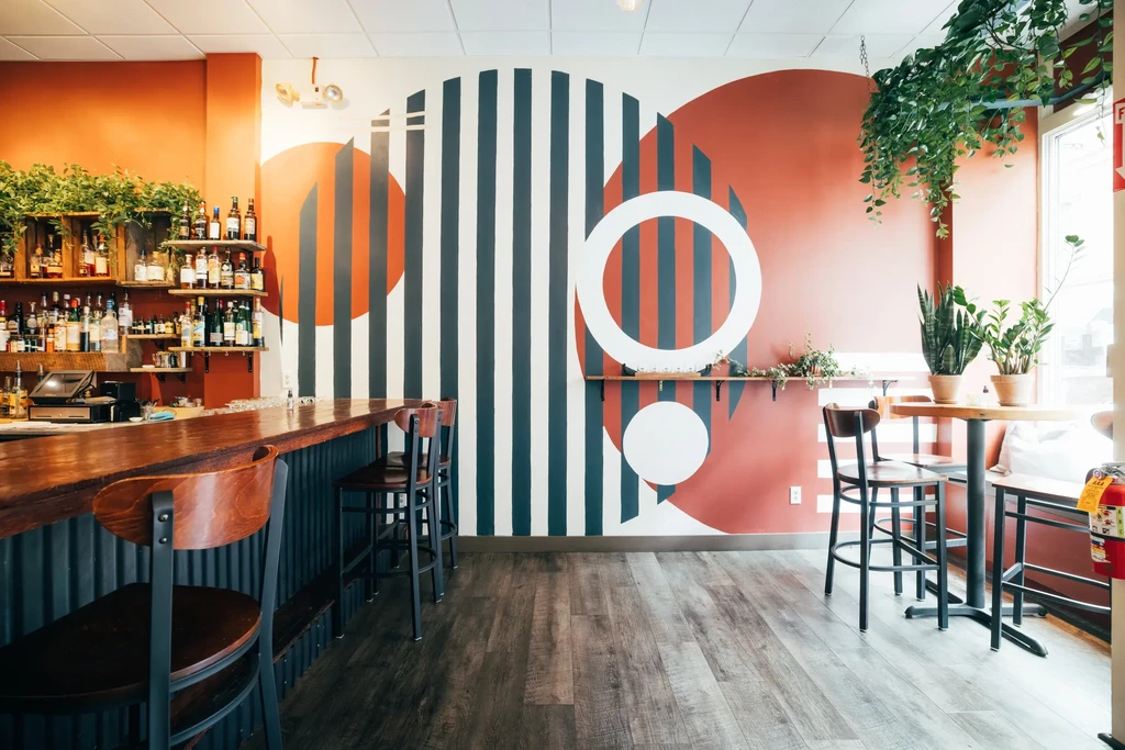 Modern bar interior with terracotta wall, geometric mural, plants.