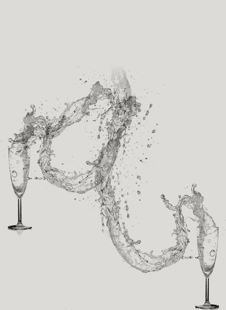 Dynamic splash of clear liquid connects two champagne flutes mid-air.