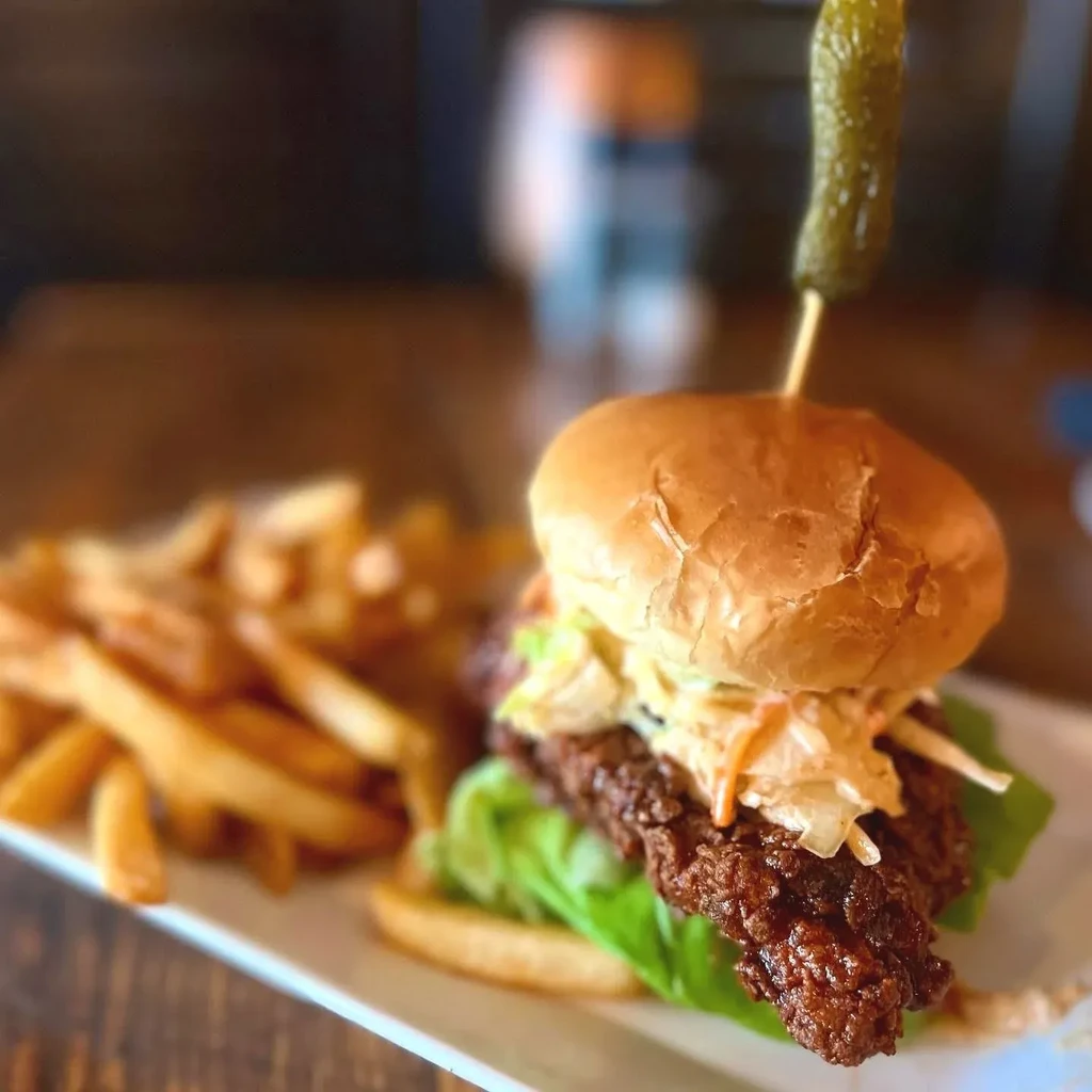 Fried chicken sandwich, brioche bun, coleslaw, pickle, and french fries.