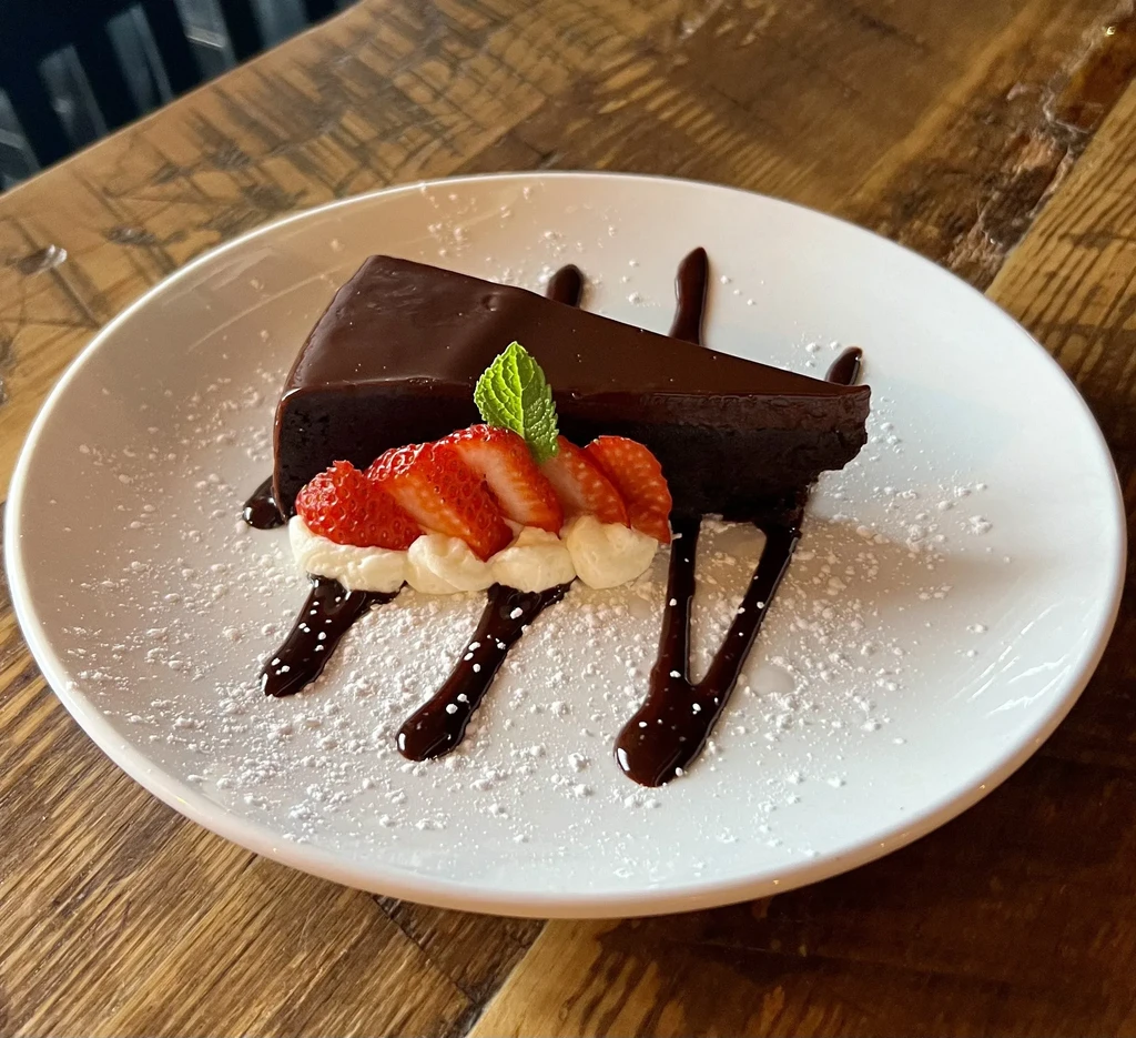 Chocolate cake with strawberries, whipped cream, and mint on a wooden table.